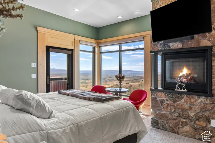 Bedroom featuring a stone-clad fireplace, extensive window line, wood-trimmed doorway, recessed lighting, and wall-mounted television