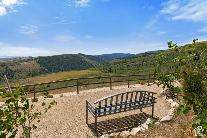 Outdoor gravel patio with a metal bench, framed by a wooden fence, overlooking a vast mountainous landscape with dense tree coverage and natural vegetation