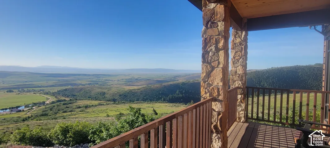 Expansive outdoor deck with natural stone columns, wood-finish railing, and broad landscape scenery