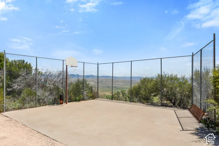 Paved outdoor court featuring a basketball hoop with a metal backboard, surrounded by chain-link fencing