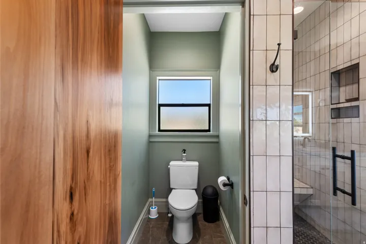 Bathroom featuring a clear glass shower enclosure, a white commode, and a window with frosted lower pane
