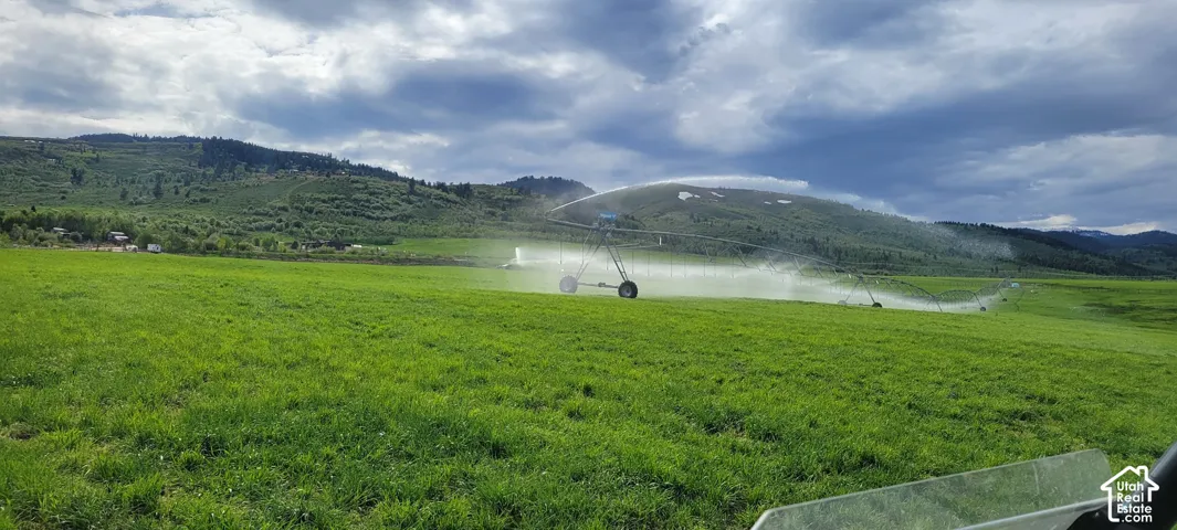 Expansive green field with an operational irrigation system, set against a backdrop of rolling hills