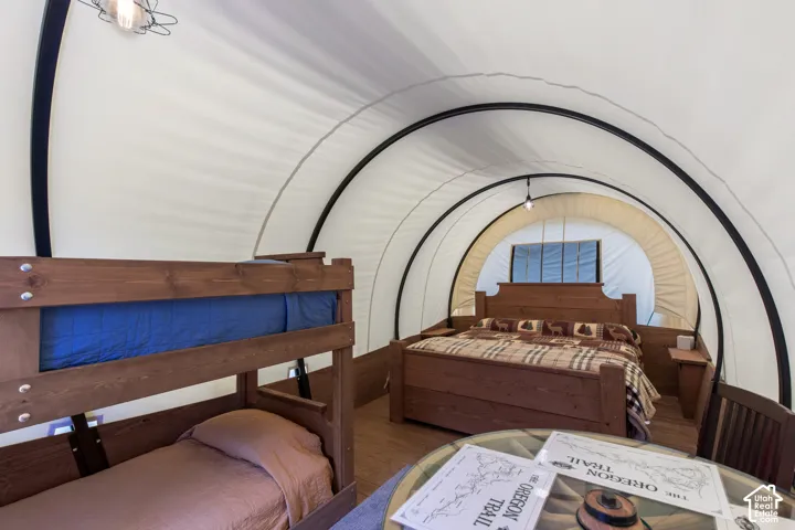 Interior space featuring wood-finish flooring, a full-size bed with a wood headboard, a bunk bed with a wood frame, a round glass-top table, and a central overhead light fixture