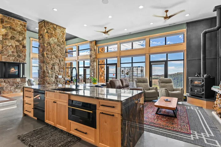 Gourmet kitchen island with an integrated sink and built-in microwave, featuring light wood cabinetry, stone-finish countertops, and an integrated dishwasher