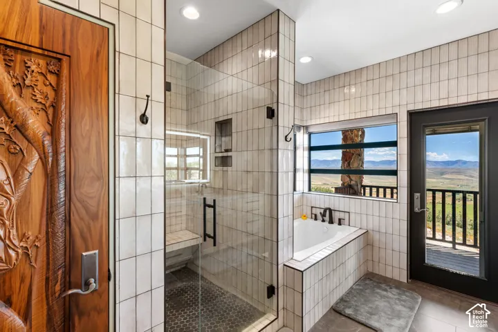 Bathroom featuring a clear glass shower enclosure, a built-in tub, white vertical tile accents, a private exterior balcony, and a carved wood door