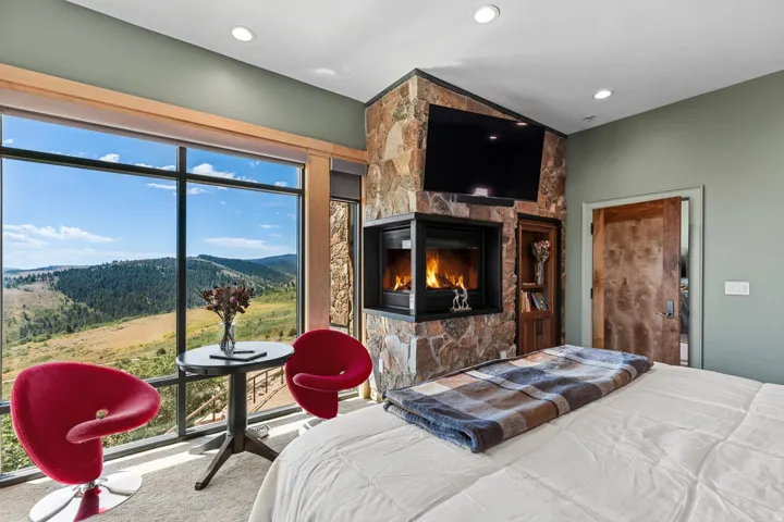 Floor-to-ceiling windows with expansive scenery, a stone-clad fireplace, built-in shelving, recessed lighting, and a solid wood door