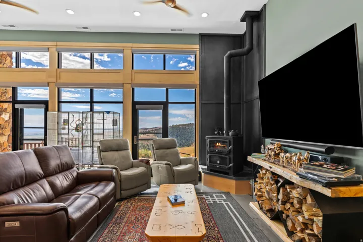 Spacious living area featuring floor-to-ceiling windows, a built-in wood-burning stove with a black metal flue, wood-finish flooring, and a built-in wood storage rack