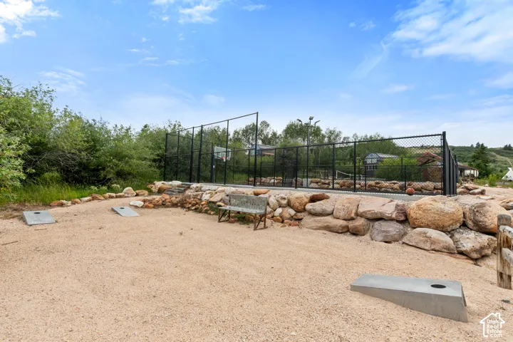 Outdoor recreational area featuring a fenced court with a basketball hoop, a gravel activity space, and a natural stone retaining wall