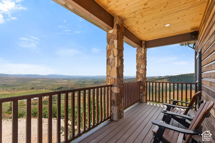 Covered deck featuring stone-clad pillars, wood-finish ceiling, and durable composite decking, overlooking expansive mountain and valley scenery