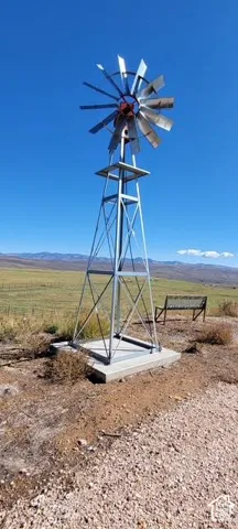Galvanized steel windmill on a concrete pad, featuring a multi-blade fan and a distant mountain range backdrop