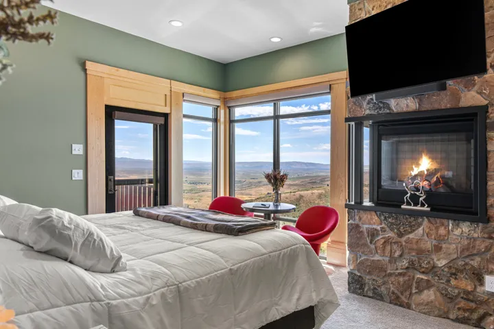 Bedroom featuring a stone-clad fireplace, extensive window line, wood-trimmed doorway, recessed lighting, and wall-mounted television