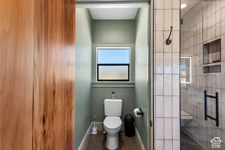 Bathroom featuring a clear glass shower enclosure, a white commode, and a window with frosted lower pane