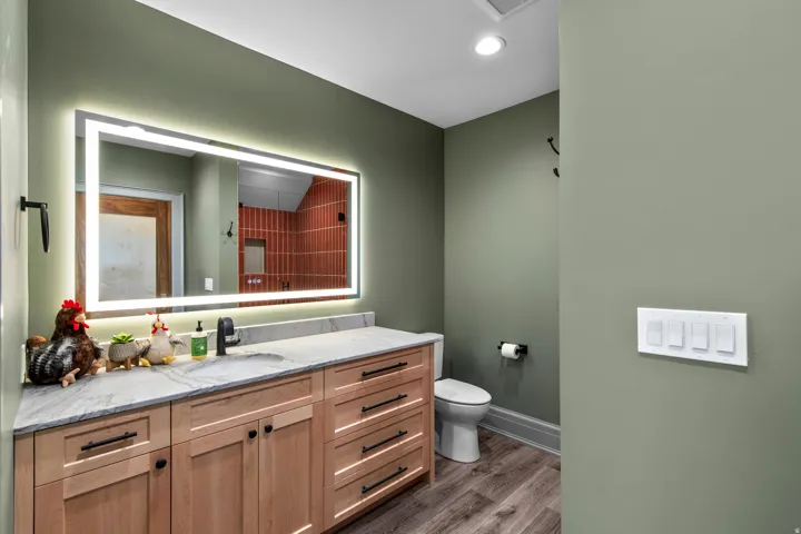 Bathroom featuring a light wood-finish vanity with ample storage, a light stone countertop, and a contemporary illuminated mirror