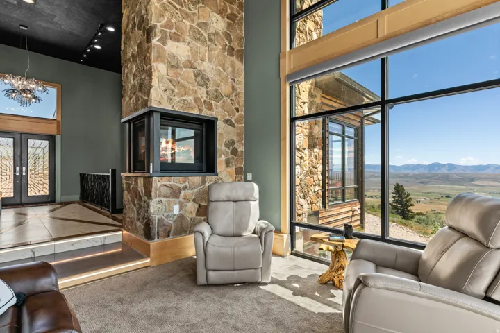 Soaring stone fireplace with a built-in firebox, floor-to-ceiling windows, and a panoramic mountain landscape
