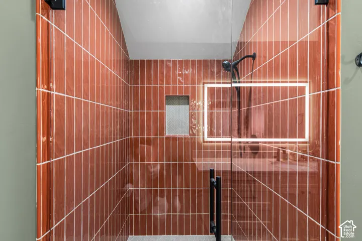 Glass-enclosed shower featuring vertically-stacked terracotta-hued wall tiles, black matte fixtures, and a recessed tiled niche