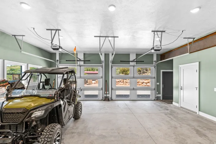 Spacious garage featuring a concrete floor, two overhead garage doors with frosted and clear glass panels, multiple recessed ceiling lights, and two interior doors