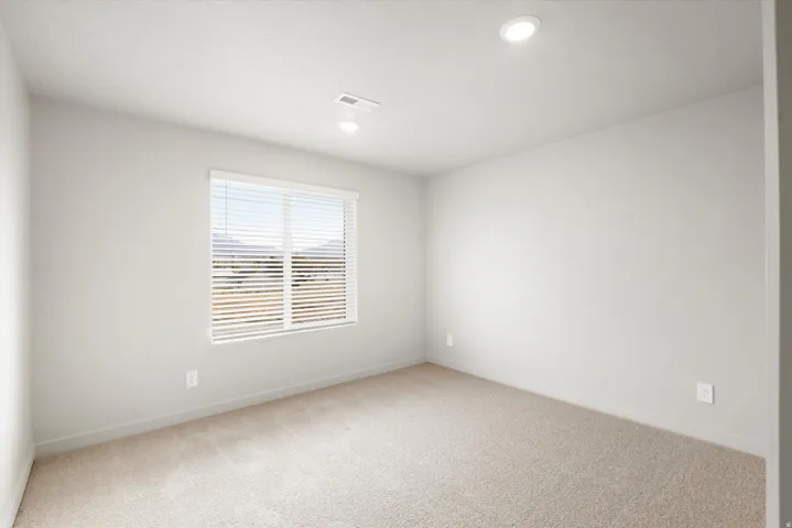 Bright room featuring a window with horizontal blinds, neutral-toned carpeting, recessed ceiling lighting, and a neutral wall color