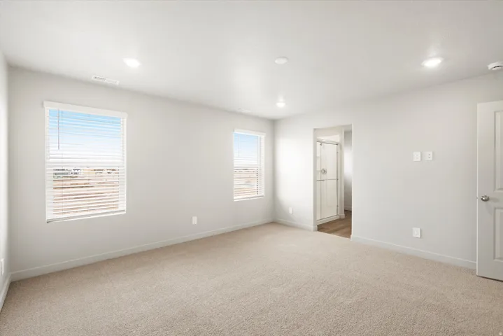 Spacious carpeted room featuring two windows with blinds, recessed lighting, and a doorway opening to a shower with a glass enclosure