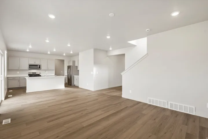 Open-concept living area featuring wood-finish flooring, recessed lighting, and a modern kitchen with light gray cabinetry, stainless steel appliances, and a central island