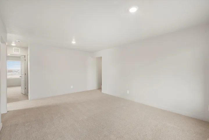 Spacious room featuring neutral carpeting, light-toned walls, and recessed lighting
