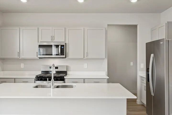 Contemporary kitchen featuring an island with an undermount double basin sink, light-toned cabinetry, stainless steel appliances, white countertops, and recessed lighting