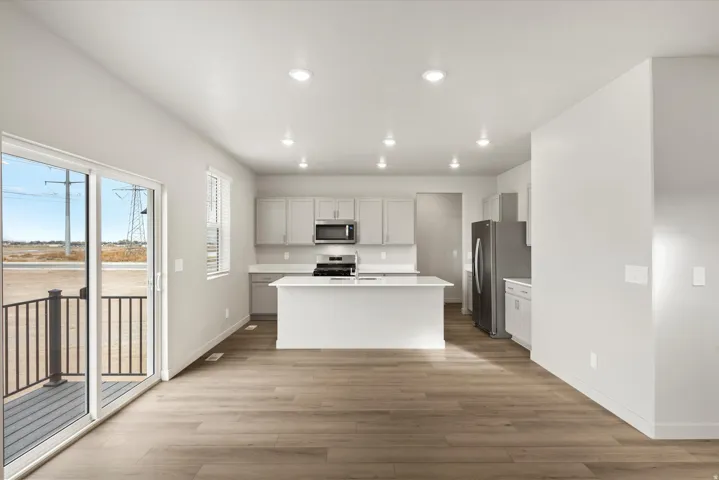 Open-concept living area featuring wood-finish flooring, a contemporary kitchen with a central island, stainless steel appliances, and a sliding glass door leading to an outdoor deck