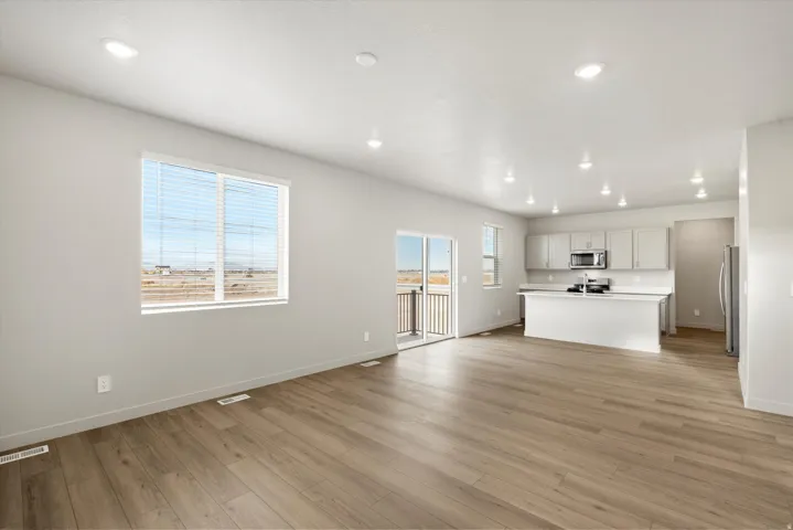 Open-concept living space featuring wood-finish flooring, recessed lighting, and a sliding glass door leading to a balcony