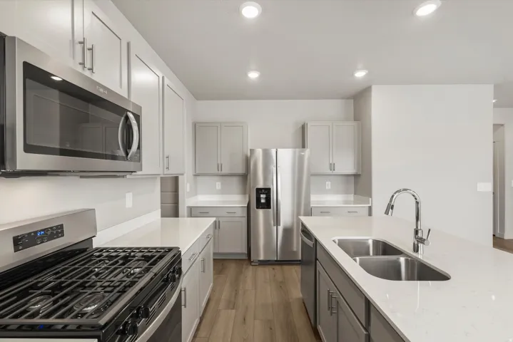 Contemporary kitchen featuring light wood-finish flooring, stainless steel appliances, light gray cabinetry, and white countertops