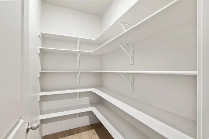 Walk-in pantry featuring expansive white shelving, a light wood-finish floor, and a white interior door with a brushed nickel knob