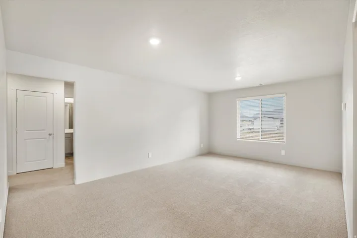 Spacious room featuring neutral carpeting, a large window with blinds, recessed lighting, and a two-panel interior door
