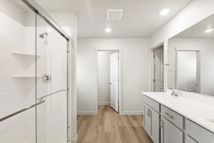 Contemporary bathroom featuring a glass-enclosed shower with white subway tile, a dual-sink vanity with light gray cabinetry, and wood-finish flooring