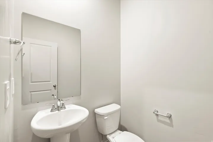 Pedestal sink with chrome faucet, large wall-mounted mirror, and white toilet