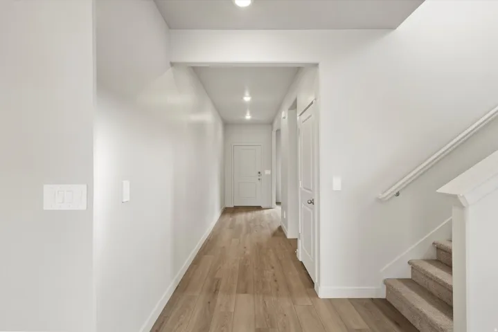 Hallway featuring wood-finish flooring, recessed lighting, white trim, and a staircase with carpeted treads