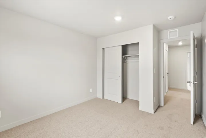 Neutral-toned room featuring light beige carpeting, white walls, and a closet with white sliding doors