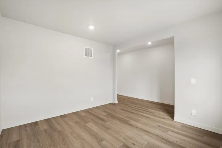 Spacious room featuring wood-finish flooring, recessed lighting, white baseboards, and neutral wall tones