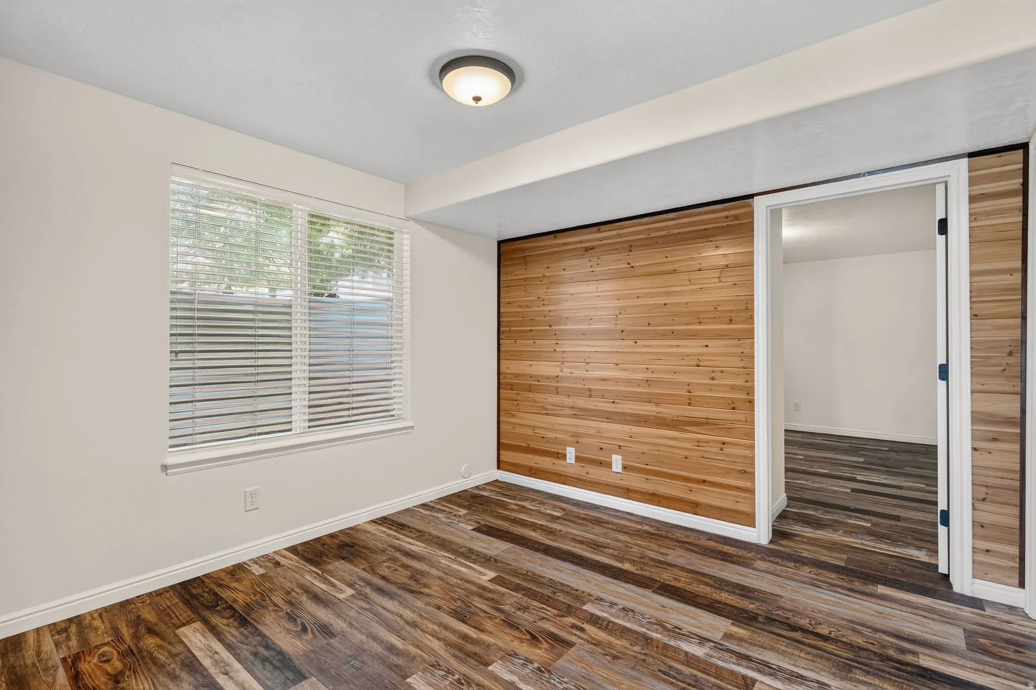 Room featuring wood-finish flooring, a prominent wood-paneled accent wall, and white trim throughout