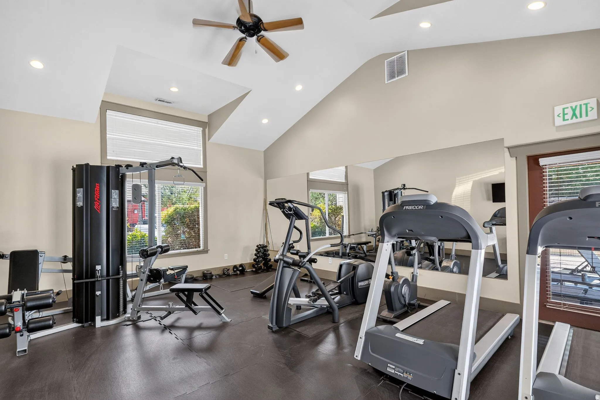 Interior fitness area featuring vaulted ceilings, recessed lighting, a ceiling fan, large windows, and wall-mounted mirrors