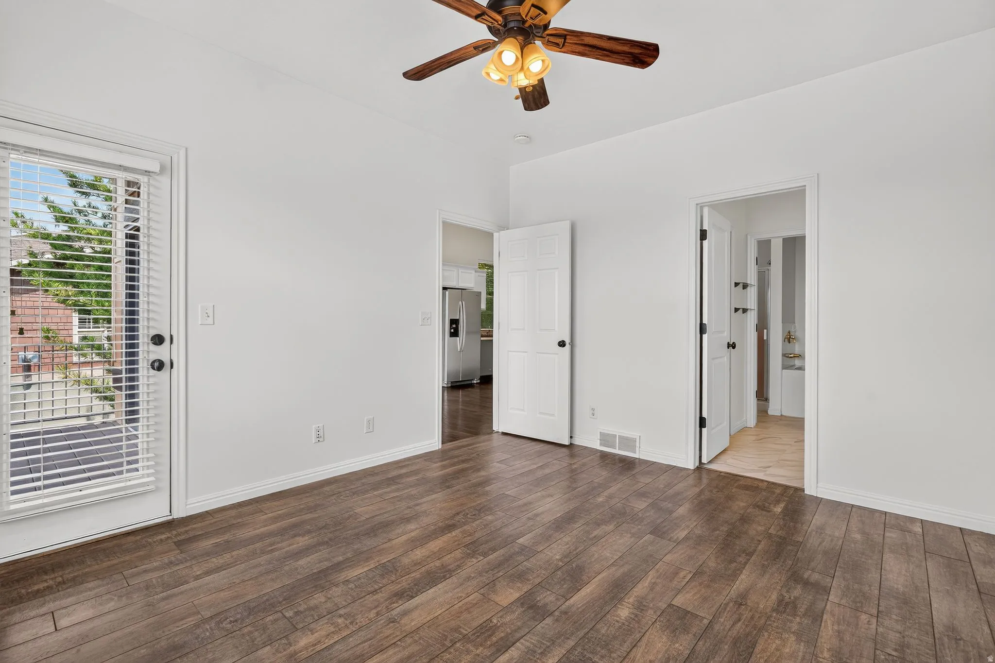 Spacious room featuring wood-finish flooring, white walls, and a ceiling fan with integrated lighting
