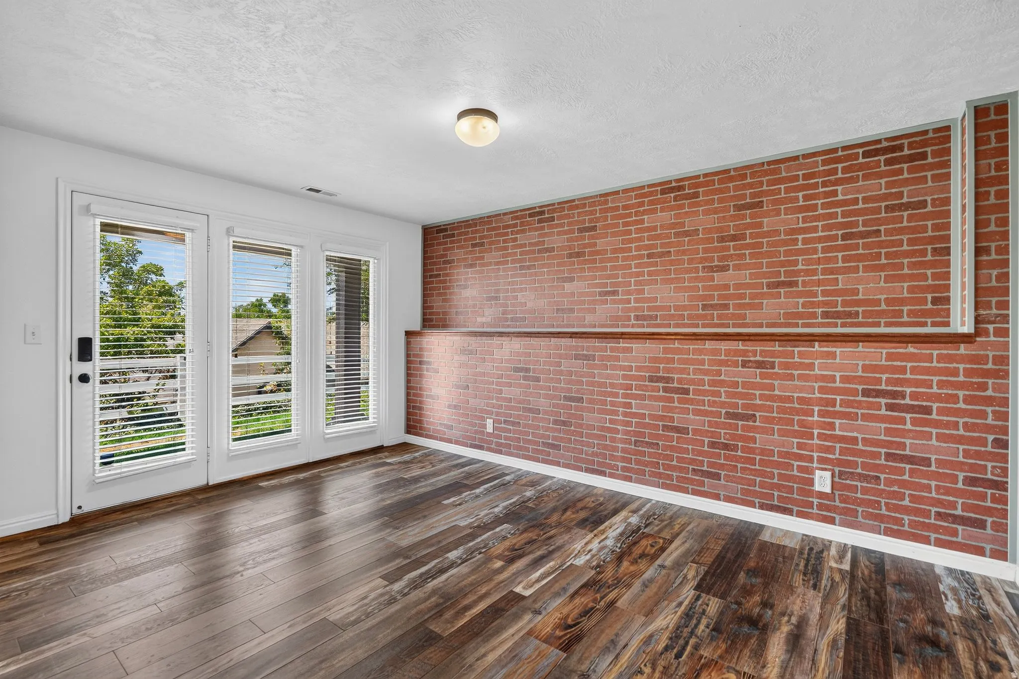 Wood-finish flooring throughout, complemented by a brick accent wall with a wood ledge