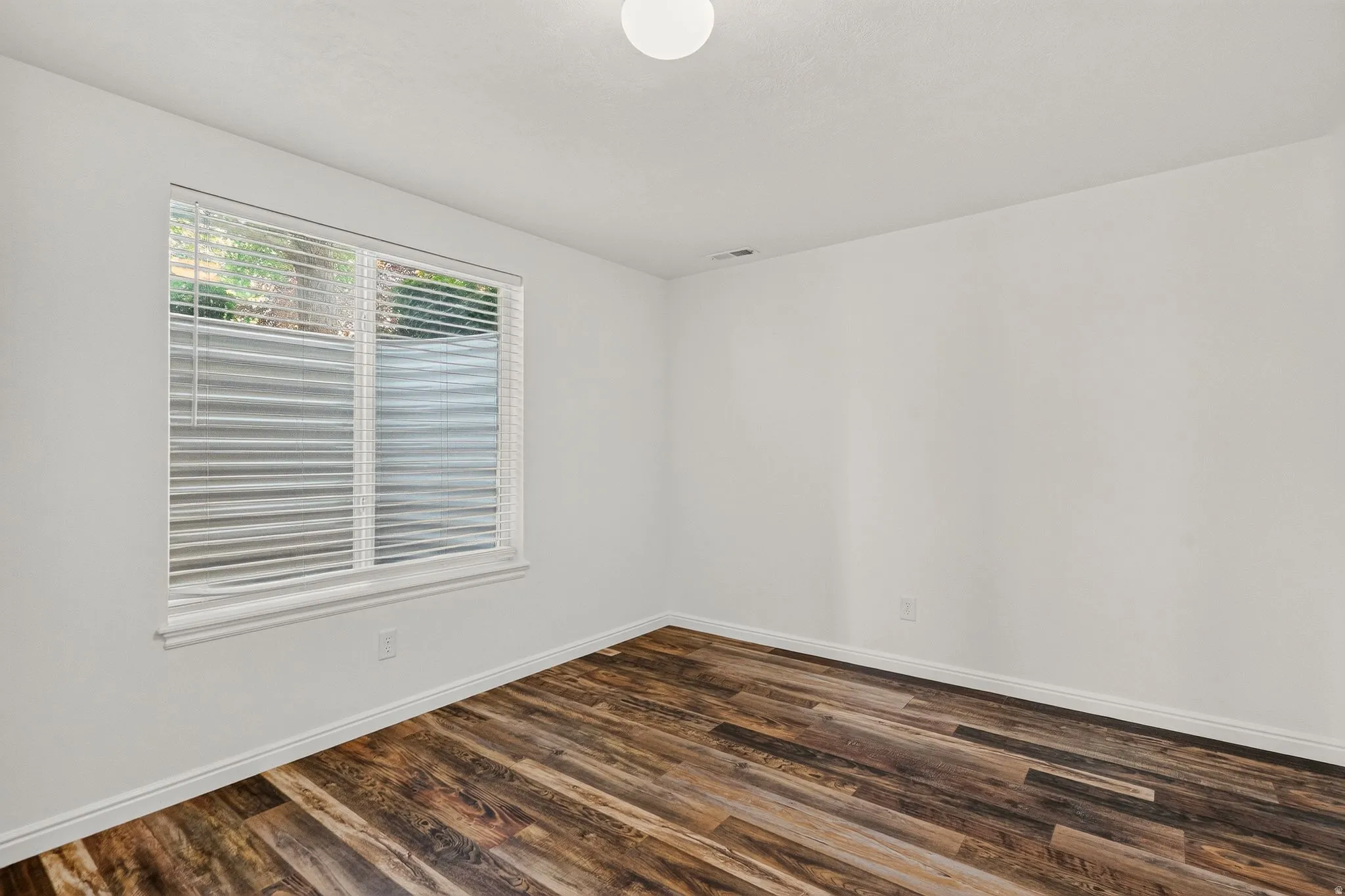 Bright room featuring wood-finish flooring, white baseboards, a single window with blinds, and clean white walls
