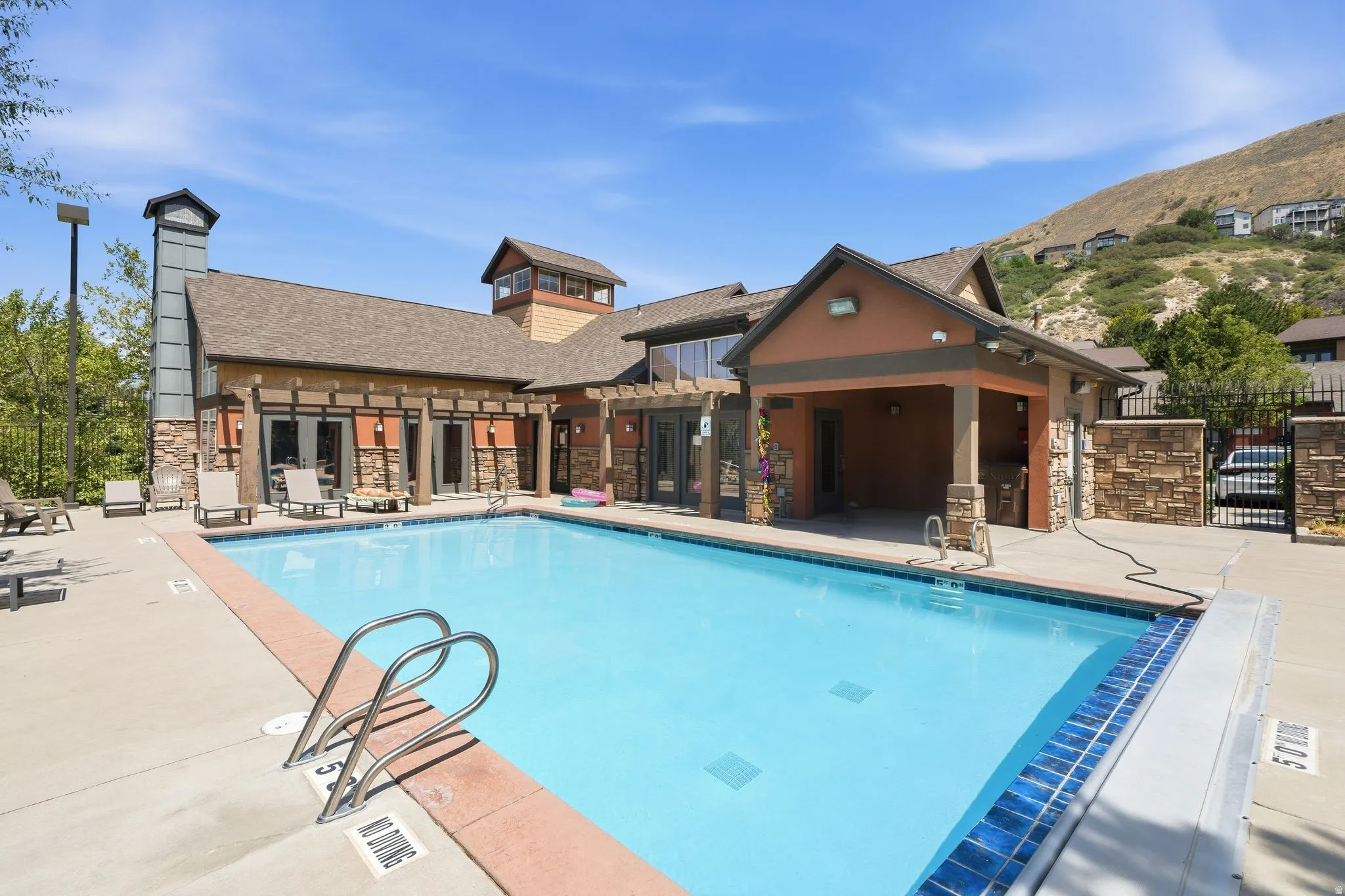 Outdoor swimming pool with concrete decking, a surrounding stone and stucco building, and a distant hillside backdrop
