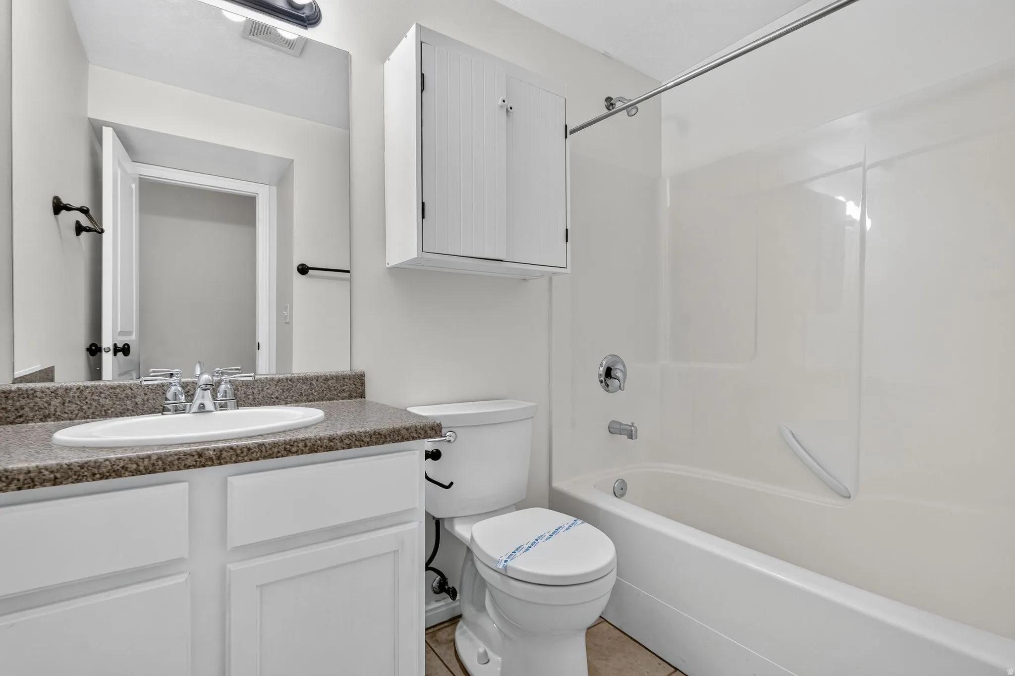 Bathroom featuring a white vanity with a speckled countertop, an integrated sink, a wall-mounted medicine cabinet, and a white tub/shower combination with chrome fixtures
