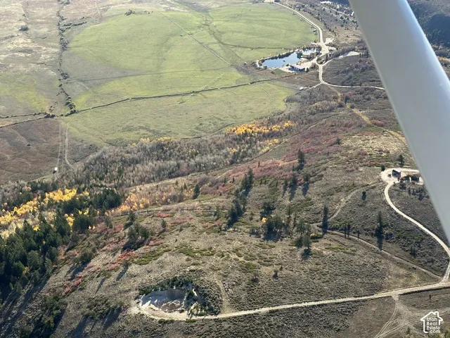 Expansive property featuring varied terrain, a large circular irrigated field, a natural pond, and multiple structures