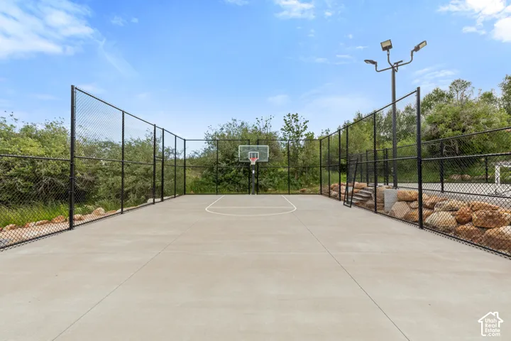 Private concrete sport court featuring an adjustable basketball hoop, perimeter fencing, and integrated lighting