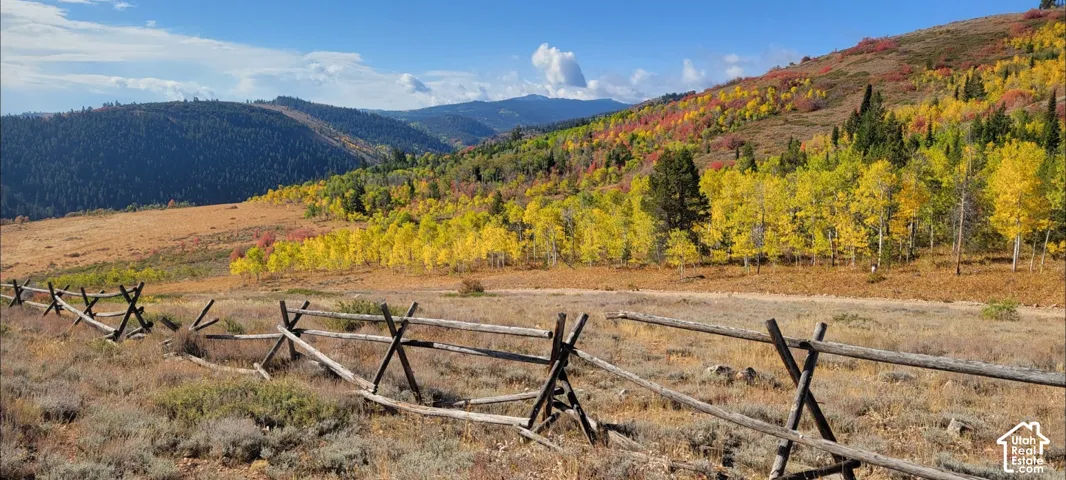 Split-rail fence delineating property boundary with expansive natural terrain featuring varied autumn foliage and distant mountain range