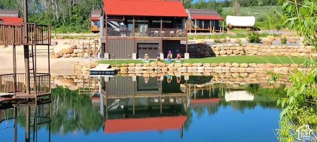 Waterfront property featuring a two-story structure with a red metal roof, a second-story balcony, and a ground-level garage door