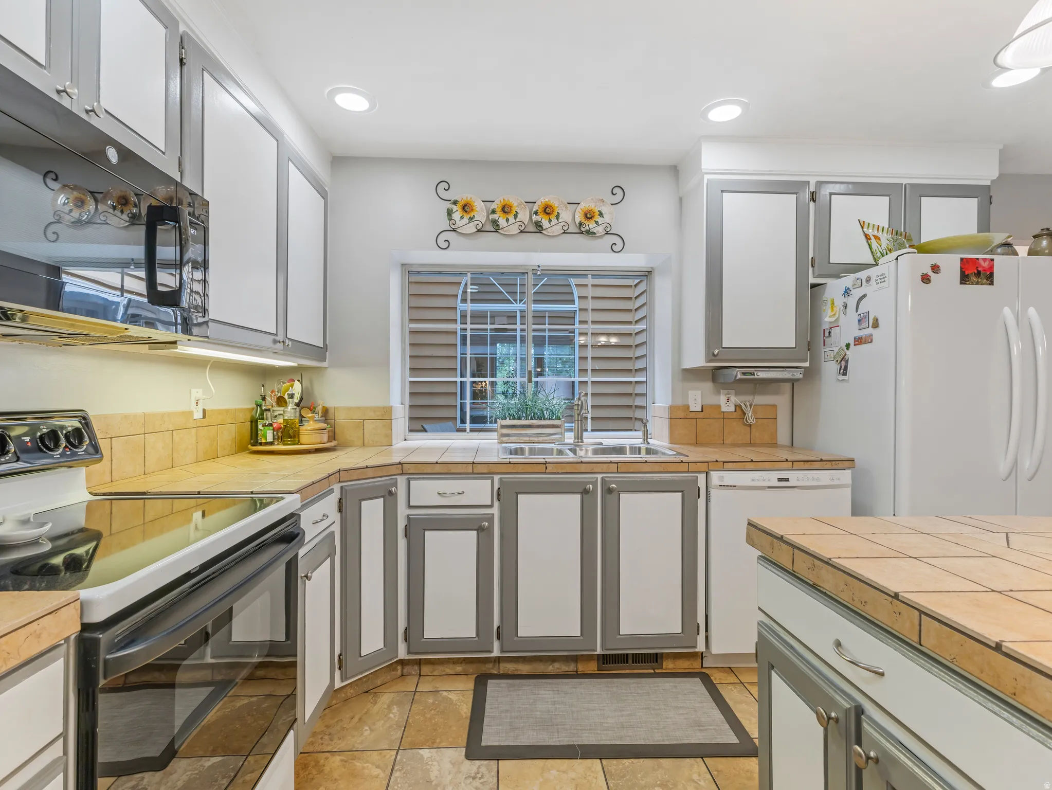 Kitchen featuring tile countertops and backsplash, white cabinetry with gray trim, a dual basin stainless steel sink, and recessed lighting