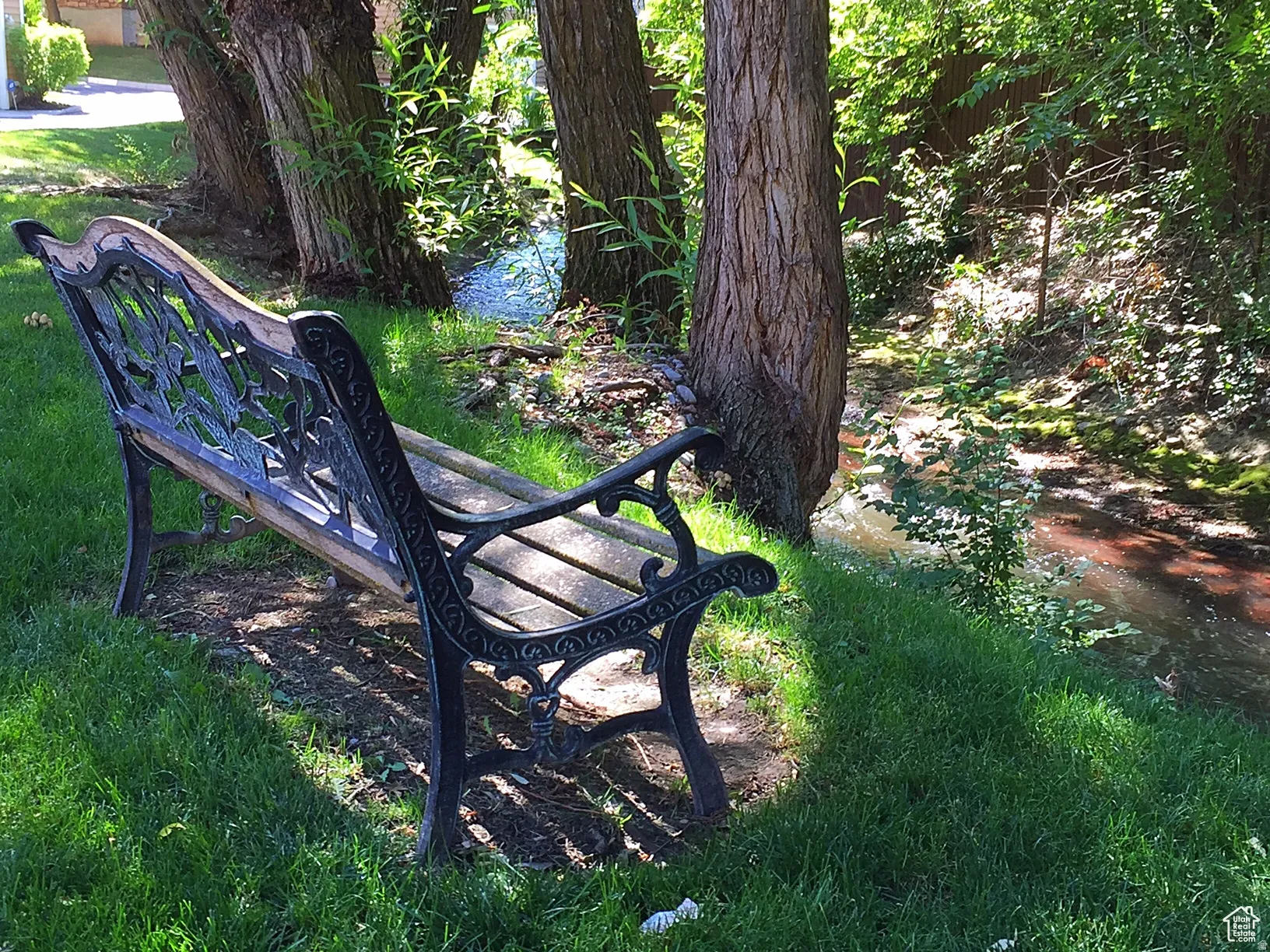 Lush green lawn with mature trees bordering a flowing stream