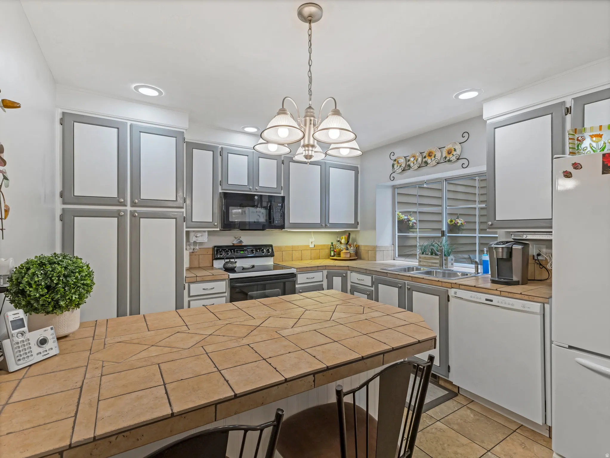 Spacious kitchen featuring two-toned cabinetry, a tiled breakfast bar, recessed lighting, and a window above the sink