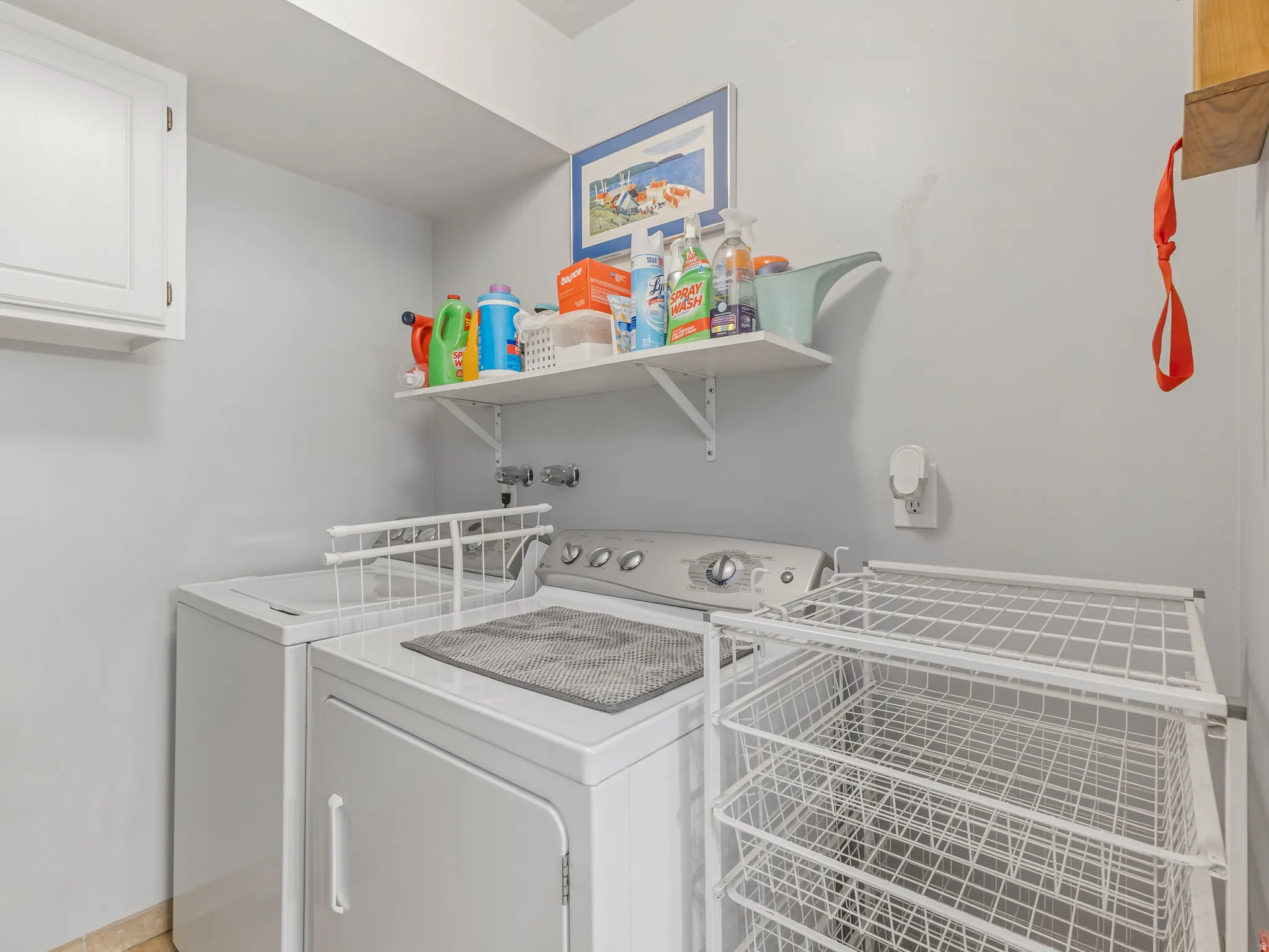 Dedicated laundry area featuring white cabinetry, a floating wall shelf, and light-toned walls